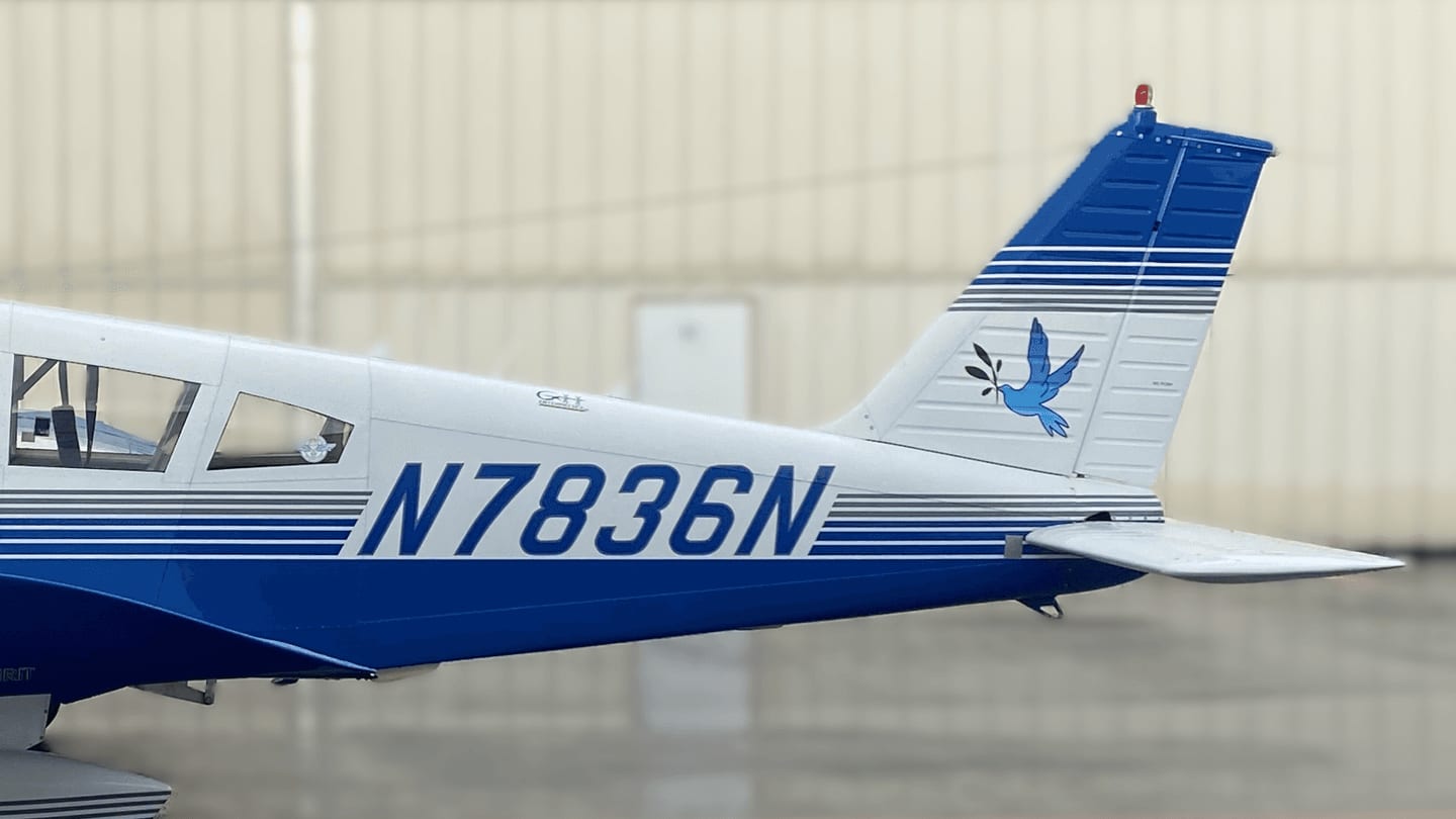Close view of Piper Cherokee N7836N’s tail, with the blue dove on the fin and the registration N7836N in royal blue along the fuselage