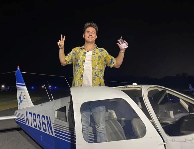 A smiling pilot standing up through the open cockpit of Piper Cherokee N7836N on the ramp at night